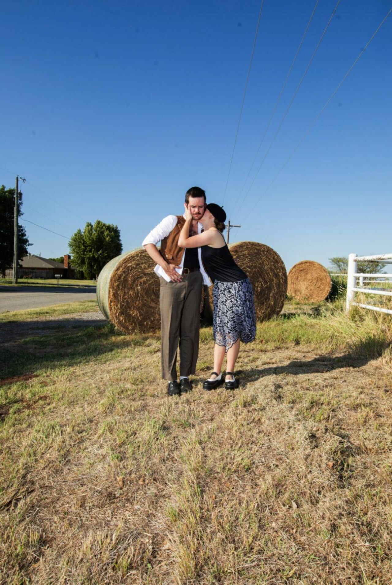 two people standing outdoors on a sunny farm in costumes from mid-20th century